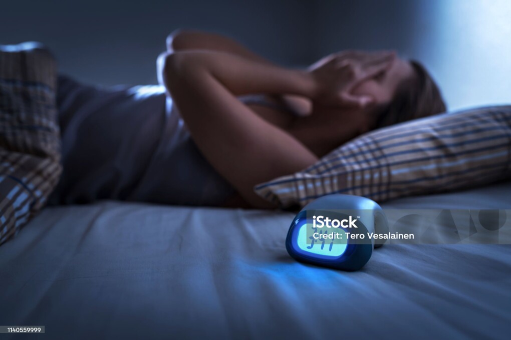 Sleepless woman suffering from insomnia, sleep apnea or stress. Tired and exhausted lady. Headache or migraine. Awake in the middle of the night. Frustrated person with problem. Alarm clock with time.