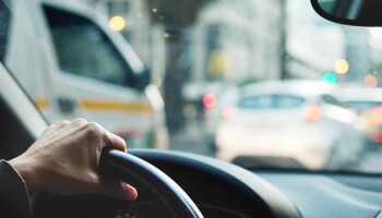 Close-up of an unrecognizable person hand on steering wheel while driving a car in city traffic
