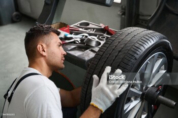 Mechanic in protective clothes and gloves standing near wheel and testing it in garage