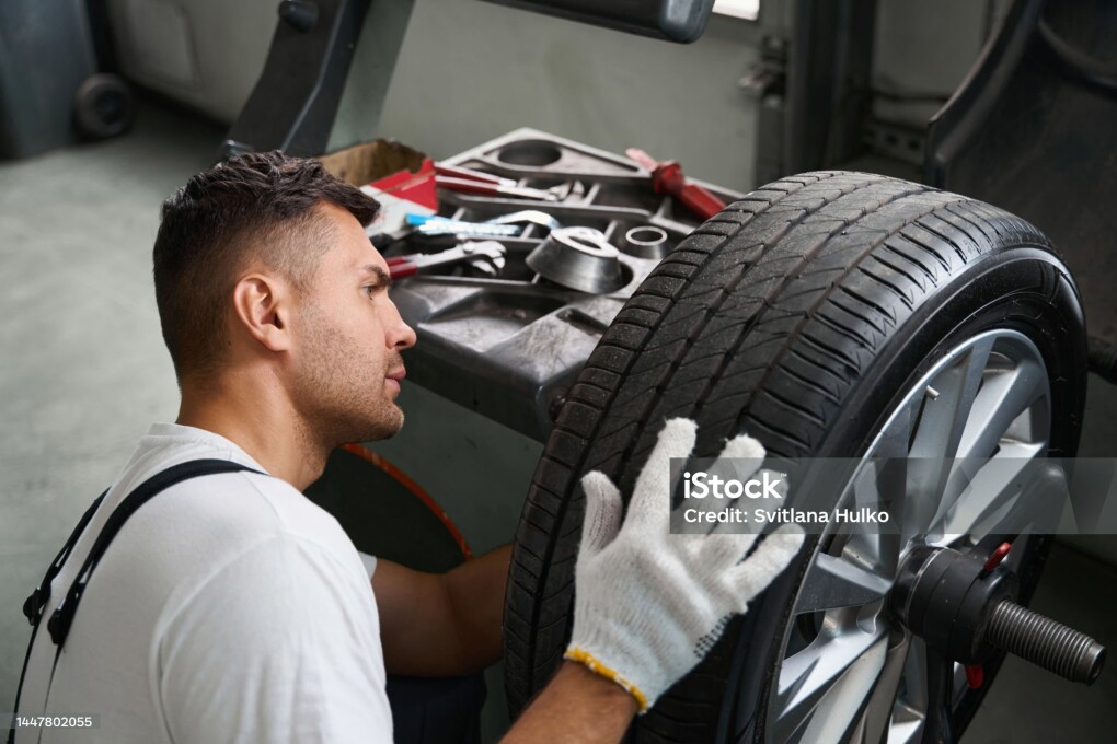 Mechanic in protective clothes and gloves standing near wheel and testing it in garage