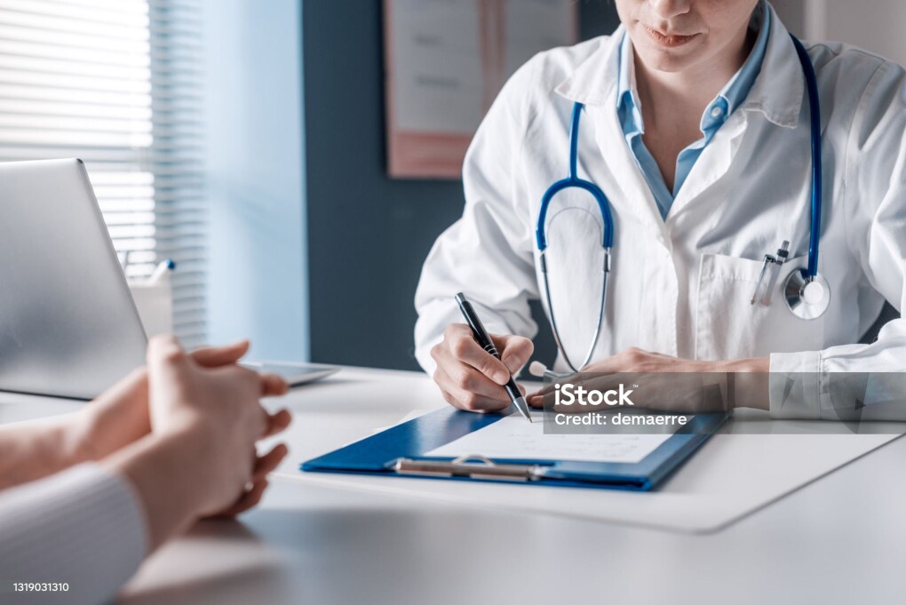 Doctor sitting at desk and writing a prescription for her patient