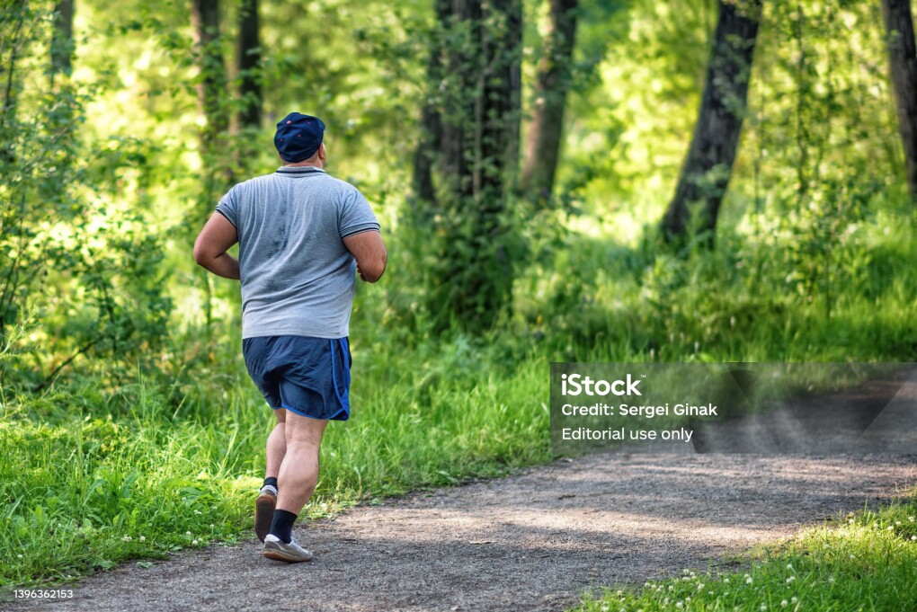 An overweight man running in a park to lose weight on summer morning: Abakan, Russia - July 26, 2020