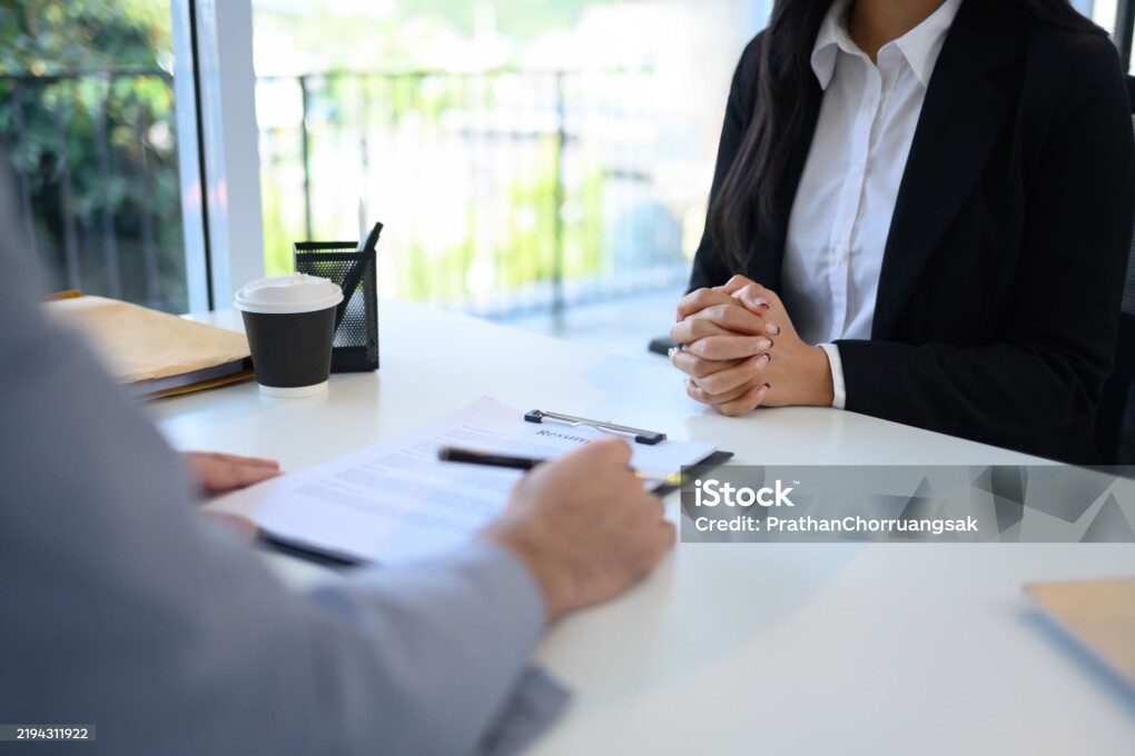 Candidate in formal wears attentively sitting across from an interviewer reviewing her resume.
