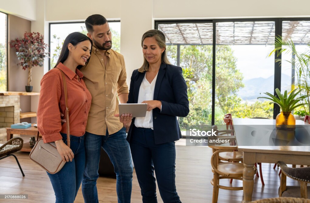 Real estate agent using a digital tablet to show pictures of a house to a couple at a showing