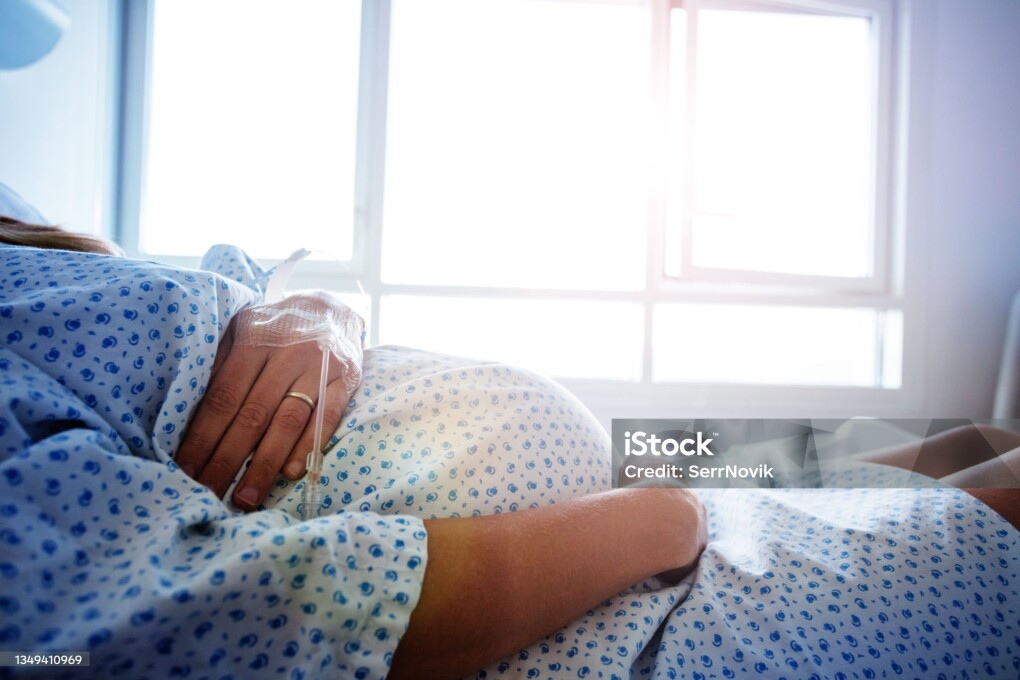 Close-up of a pregnant woman's belly in the hospital bed with catheter in hand