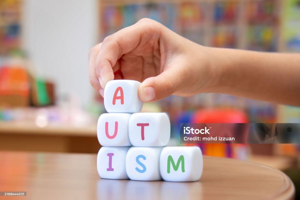 A child's hand placing a white cube with the letter A on top of a pyramid of cubes spelling AUTISM, highlighting awareness and understanding of autism spectrum disorder.