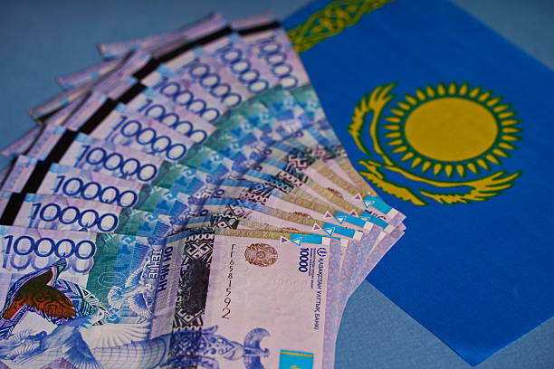 Tenge banknotes are laid out on the table, against the background of the flag of Kazakhstan.