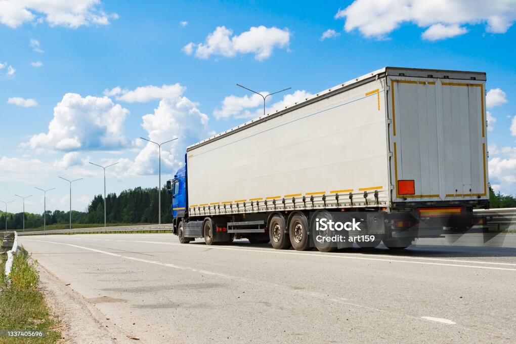 A heavy-duty vehicle with a semitrailer drives along the highway on a summer day.
