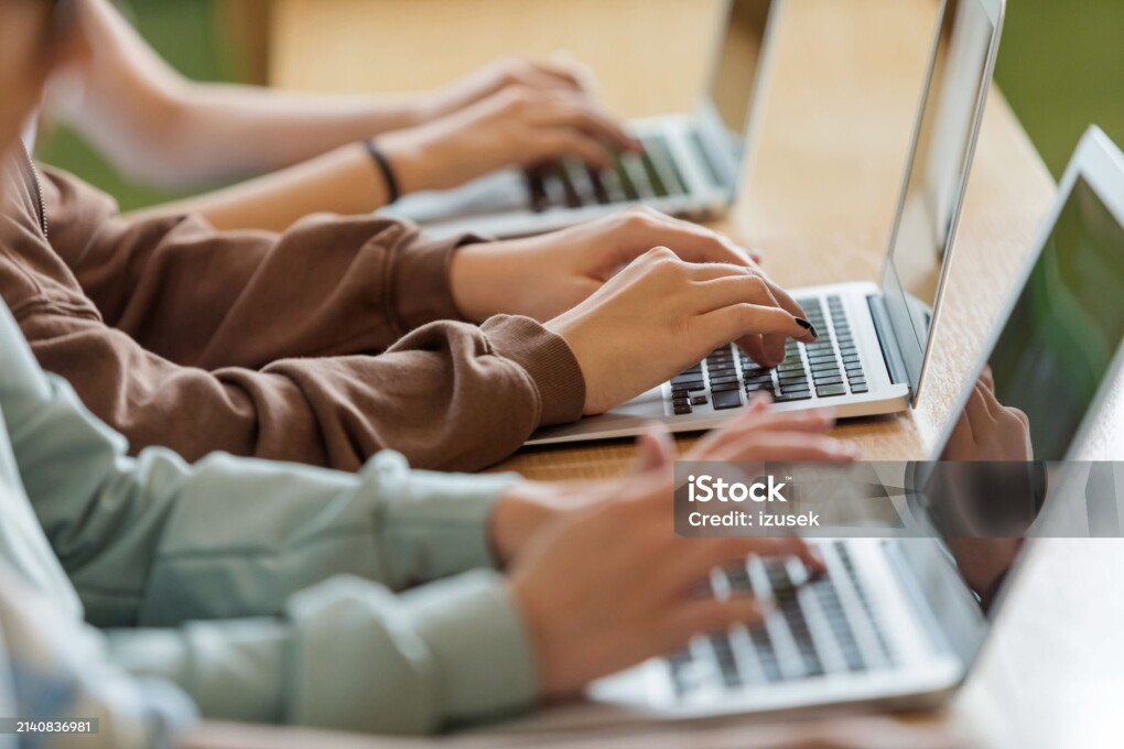 High school students sitting at the desk in the classroom during lesson, using laptops. Close up of hands, unrecognizable people.