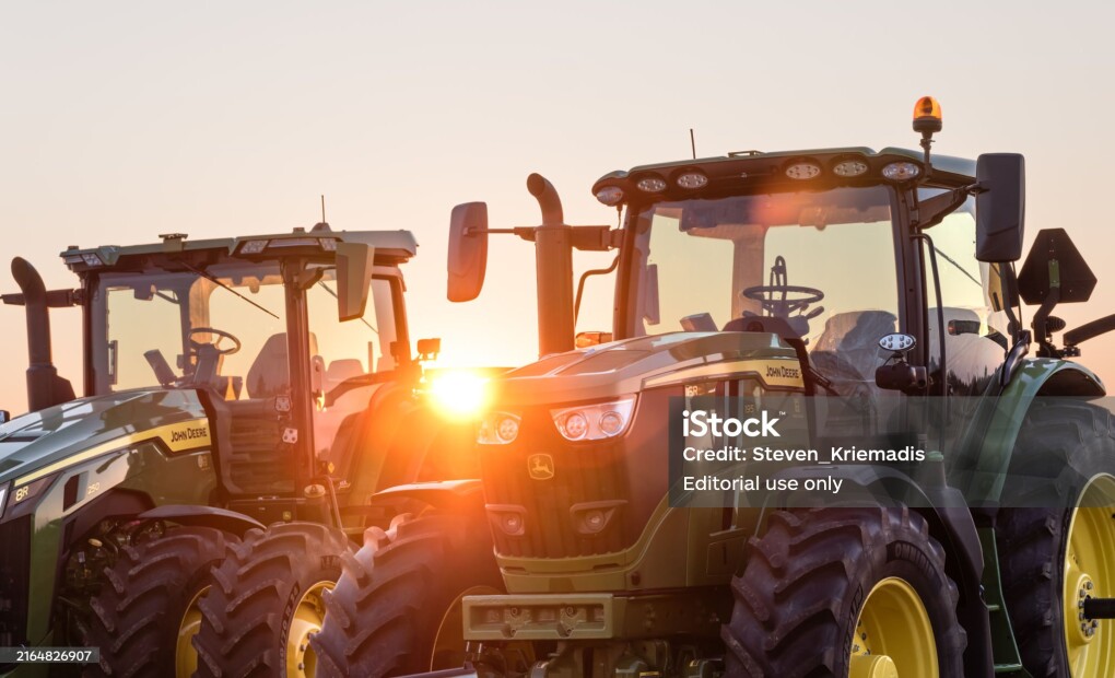 Kingsville, Ontario, Canada - July 27, 2024: Two John Deere farm Tractors silhouetted against the setting sun.