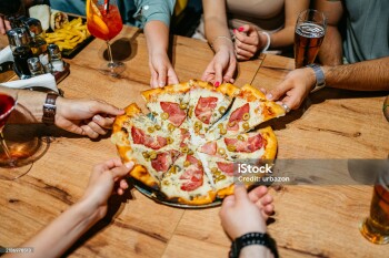 High-angle view of six young people taking a slice of pizza in a pub.
