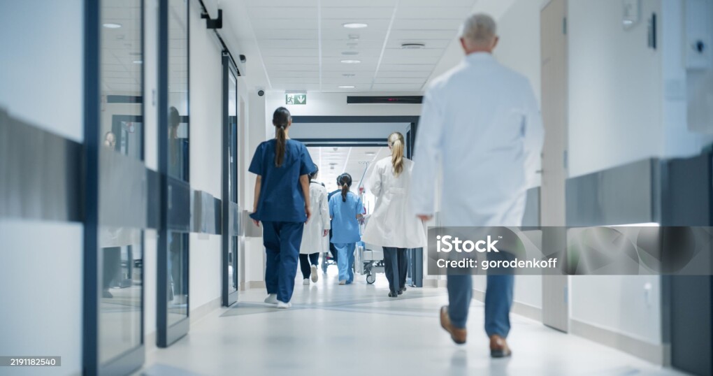 Hospital Hallway with Doctors, Nurses and Specialists in Hospital. Female and Male Physicians, Surgeons, Healthcare Officials Walk Together in Corridor with Their Back to Camera