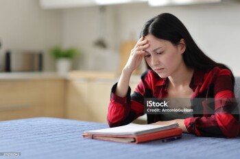 Worried asian student reading notes in the kitchen