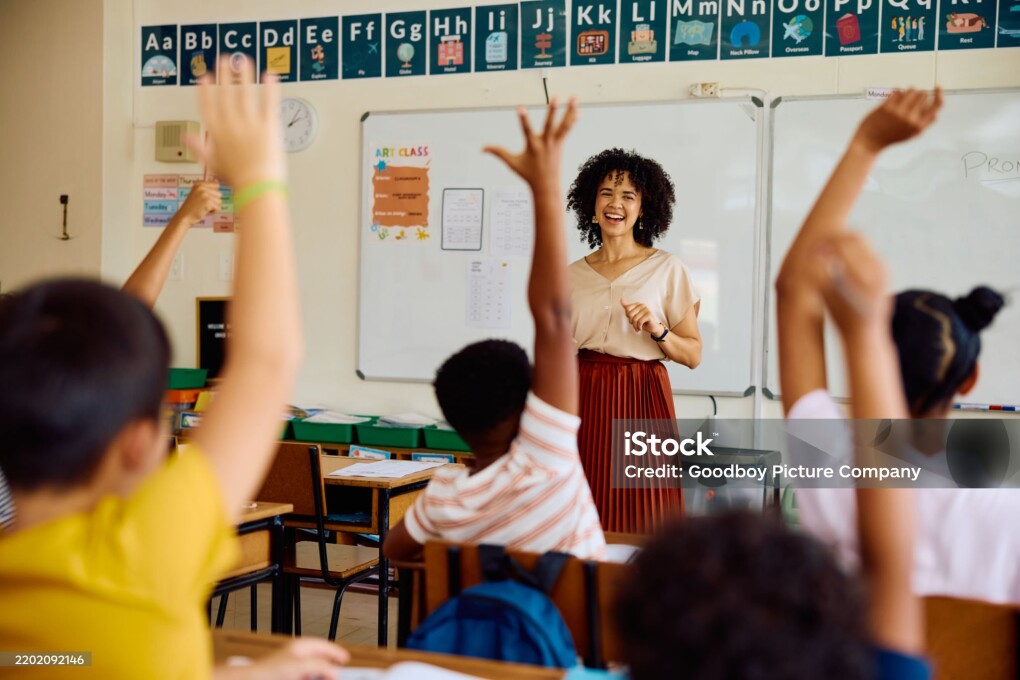 School children sitting at desks with arms up to answer question, enthusiasm, knowledge, participation