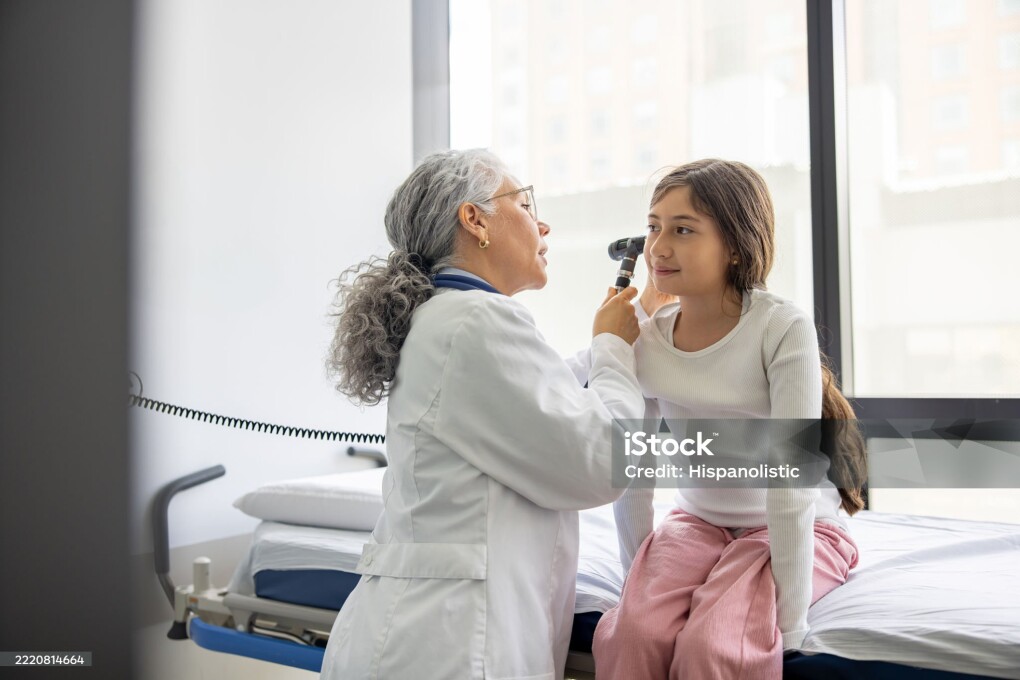 Latin American pediatrician performing an ear exam on a girl in the consultation room