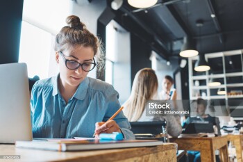 Young woman manager doing her job and researching project using laptop and paperwork in big loft office