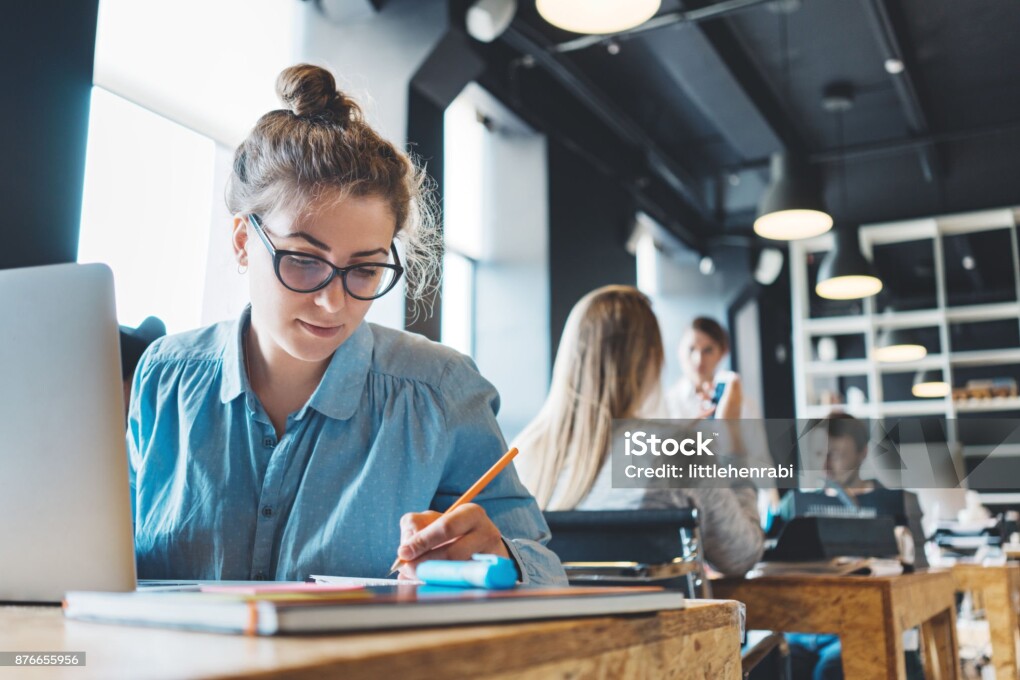 Young woman manager doing her job and researching project using laptop and paperwork in big loft office