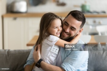Close up smiling loving young father hugging adorable little daughter, enjoying tender moment, spending weekend together, sitting on cozy couch at home, good family relationship between dad and child