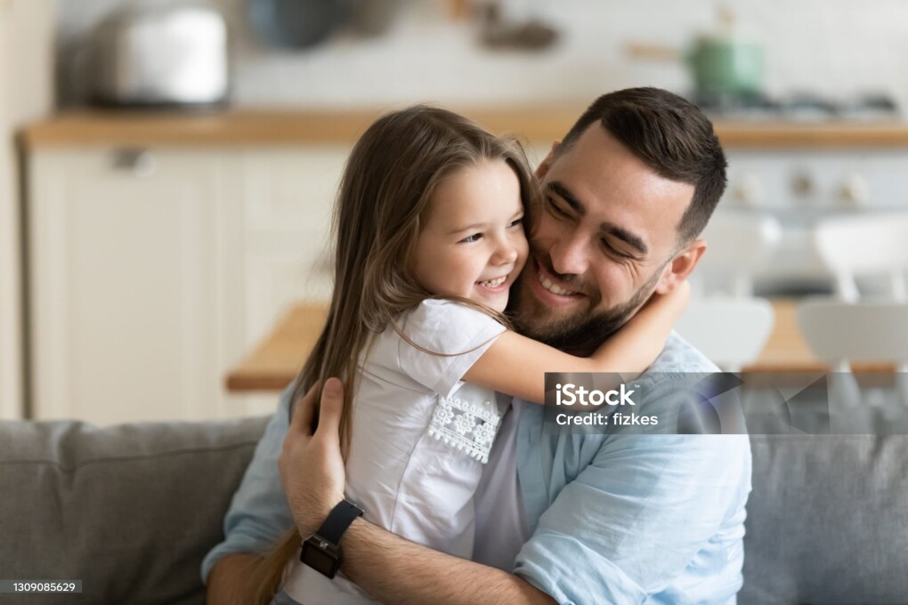 Close up smiling loving young father hugging adorable little daughter, enjoying tender moment, spending weekend together, sitting on cozy couch at home, good family relationship between dad and child