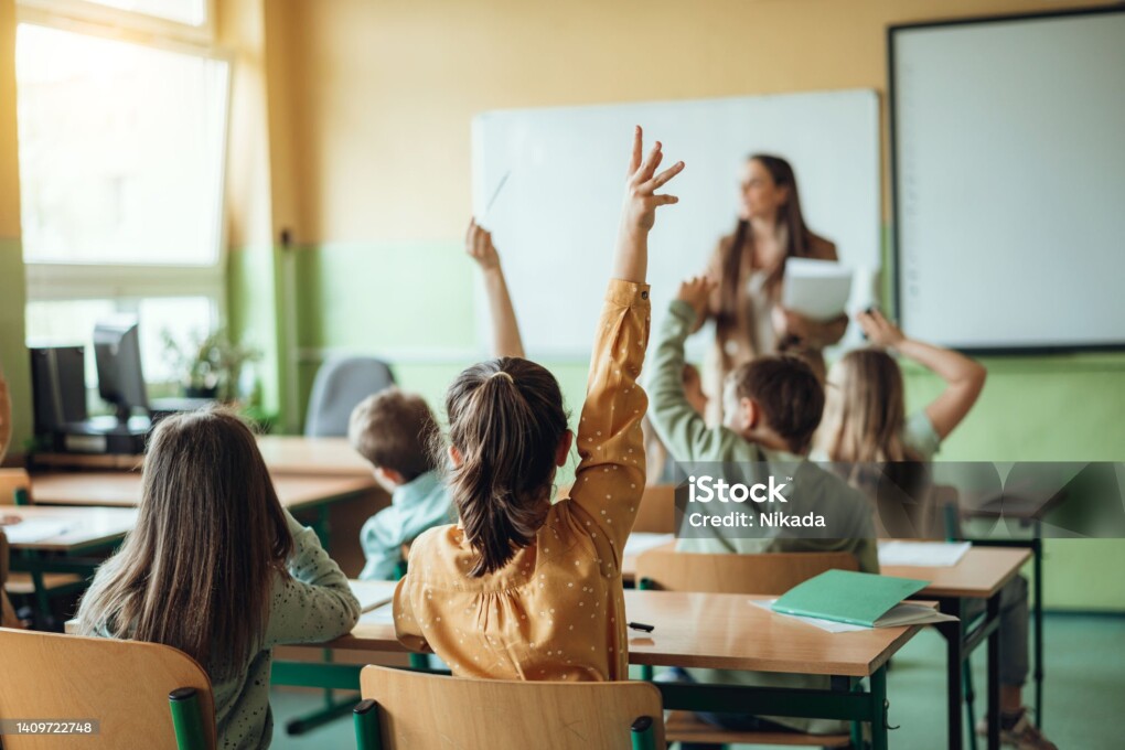 Students raising hands while teacher asking them questions in classroom