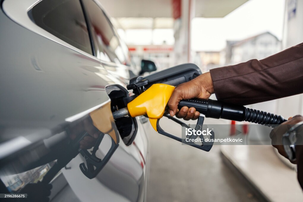 Cropped picture of an unrecognizable diverse man's hand holding nozzle and filling up the tank at gas station.