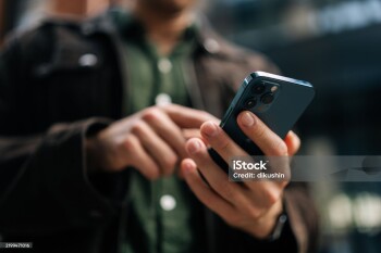 Close-up hands of unrecognizable man holding and using smartphone standing on city street, browsing internet, checking social media, using mobile application. Concept of modern communication.