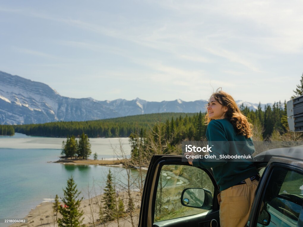 Woman looking at scenic lake along the road in Banff during road trip with SUV in springtime