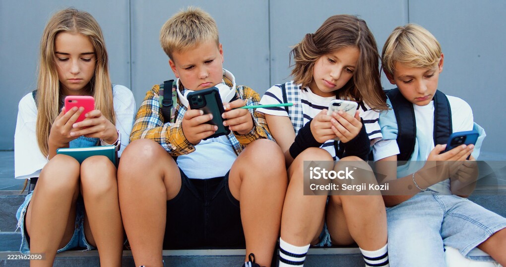 Group of teenage sad friends holding phones and browsing sitting on stairs near school building after lerning day. Happy positive teens friends texting on cellphones gadgets and talking.