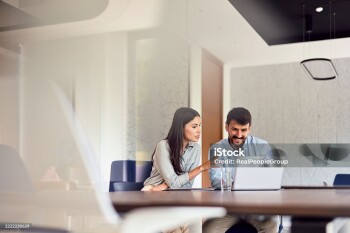 Two young professionals collaborating on a project, engaging with a laptop and exchanging ideas in a bright, modern office space filled with energy and creativity