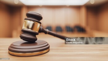 A wooden judge's gavel and sounding block on a desk with a blurred courtroom in the background. Focus on themes of law, authority, and verdicts. 3D rendering.