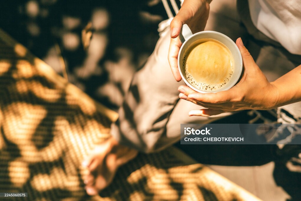 Close-up of hands holding a cup of coffee on a sunlit terrace. Warm tones, soft shadows, and relaxed morning mood perfect for wellness, lifestyle, outdoor living, and slow living themes.