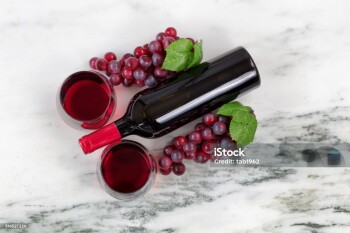 Overhead view of Red wine bottle, filled glasses and grapes on natural marble stone setting