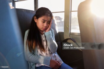 A young female student experiences motion sickness while riding the school bus. She sits alone.