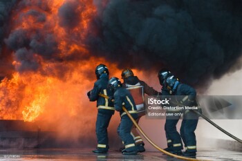 Barcelona, Cataluña, Spain - January 24, 2022: A group of firefighters facing a fire and putting it out with a hose, with smoke and heat. They are  equipped with heavy respiratory protection and wears protective equipment that protects them from the heat and flames.