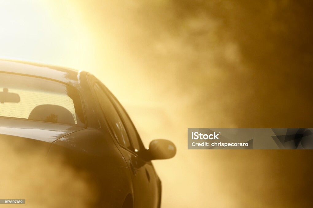 Car driving through cloud of dust on dirt road.