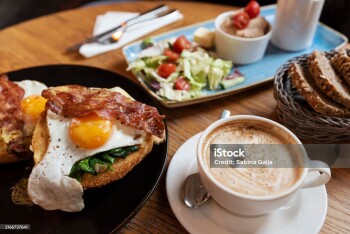 Fried egg with bacon on a plate, salad and coffee cup. English lunch in restaurant. Close-up