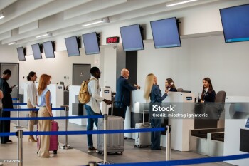 A medium multiracial group of people waiting in a check-in line at an airport terminal