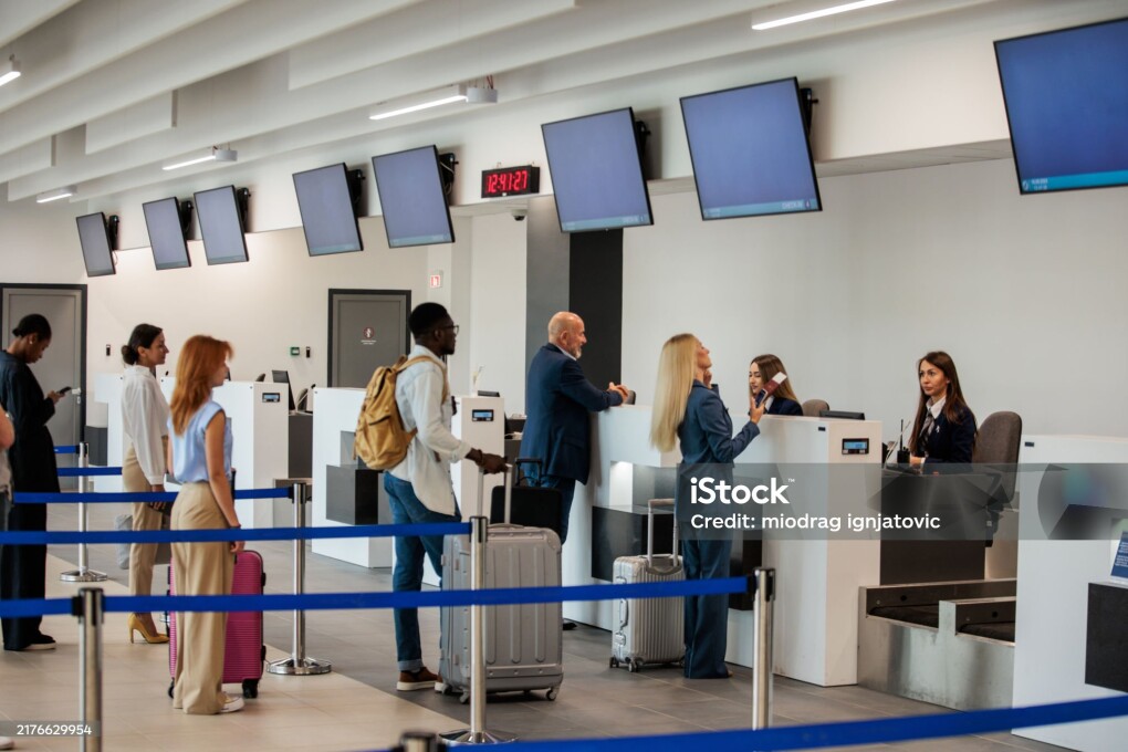 A medium multiracial group of people waiting in a check-in line at an airport terminal