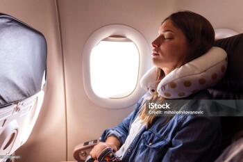 A young woman rests her head on a neck pillow and sleeps on the flight