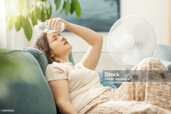 Young woman sitting on the couch at home and keeping a fresh water bottle on her forehead, she is suffering from the heat