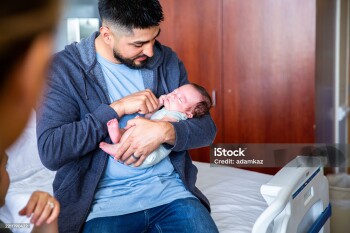 A young family consisting of a hispanic father and mother and their newborn baby boy in the hospital with grandparents, a nurse, and a pediatrician.