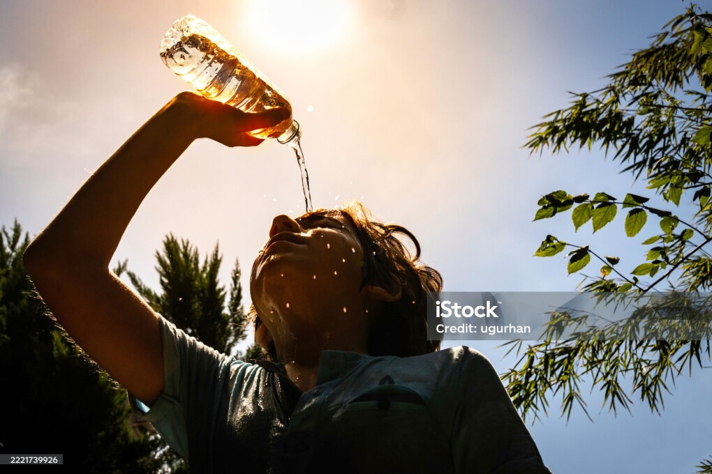 Boy pouring water on his face under the summer sun to refresh from the heat