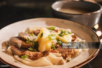 Traditional Kazakh dish beshbarmak with boiled meat, dough, potatoes and broth served on a plate, ready to be eaten