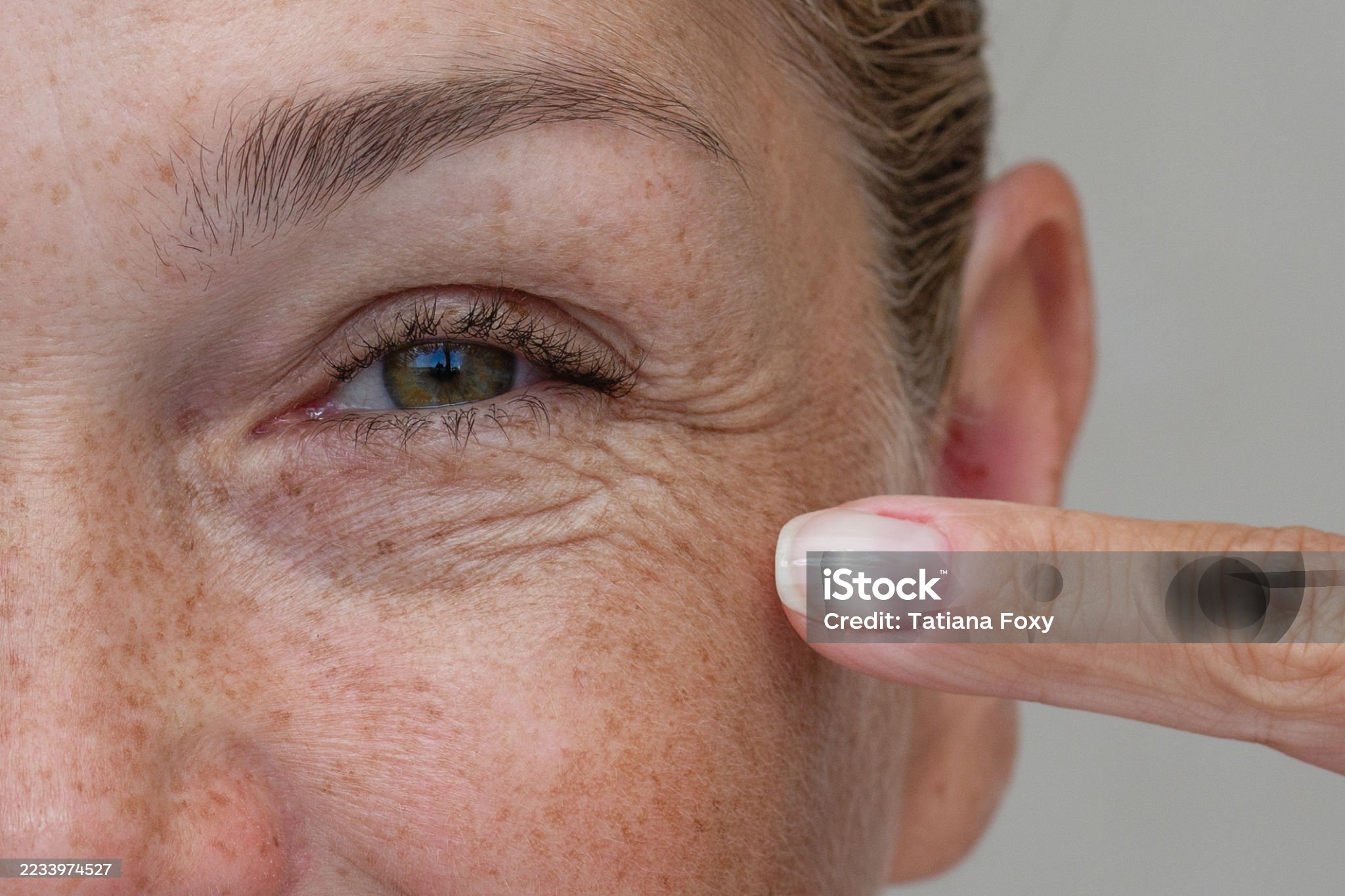Close up cropped view of a middle aged woman laughing and pointing at crows feet with her finger