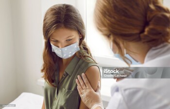 Concept of vaccination against COVID-19 for children and teenagers. Preteen girl receives injection of antiviral vaccine against coronavirus in hospital. Child in mask looks at hands of nurse.