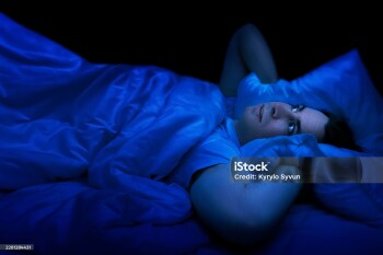 Stressed man lying awake in bed at night suffering from insomnia. Experiencing a sleepless night due to anxiety, tired fatigue, and restless thoughts in a dark bedroom. High quality photo