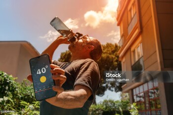 Man drinking water and holding a smartphone displaying 40°C temperature on a very hot day