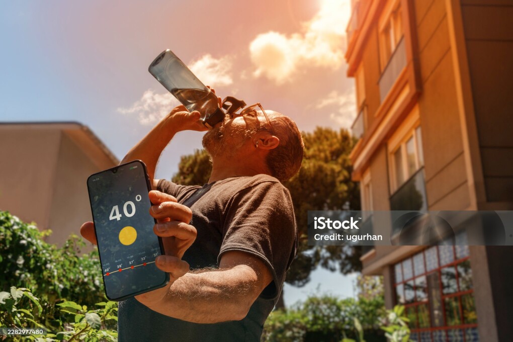 Man drinking water and holding a smartphone displaying 40°C temperature on a very hot day