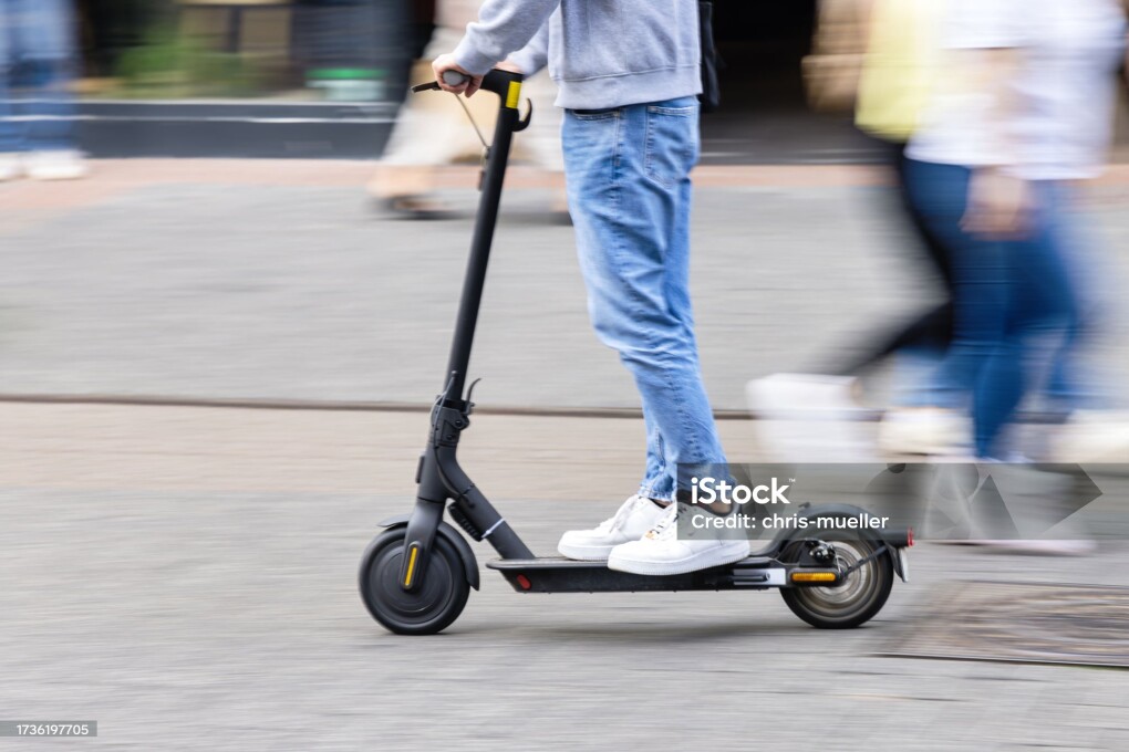 picture with intentional motion blur effect of a young person with a kick scooter in a pedestrian area