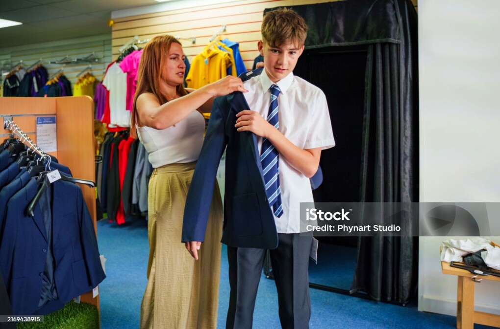 A mother and teenage son shopping new clothes for school, trying on a school uniform